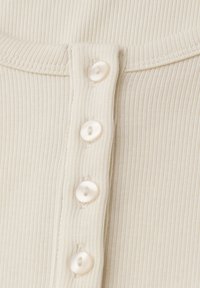 Ribbelige crèmekleurige top met een ronde halslijn en decoratieve knopen met een parelachtige afwerking langs de voorkant.