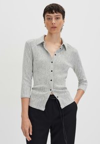 Camicia aderente con bottoni in un motivo a griglia bianca e nera. Presenta un colletto a punta e maniche a tre quarti, realizzata in un tessuto testurizzato.