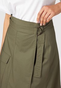 Olijfgroene rok met een brede tailleband, voorzien van een zilveren metalen ringgesp en zijzakken. Gladde stof met stikseldetails.
