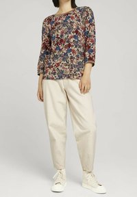 Blommönstrad topp med trekvartslånga ärmar och rund halsringning i nyanser av rött, blått och beige, tillsammans med lössittande krämfärgade byxor och vita sneakers.