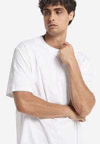 Vit bomulls-t-shirt med korta ärmar och en klassisk rund halsringning. Slät textur med en avslappnad passform, utan synliga logotyper eller mönster.