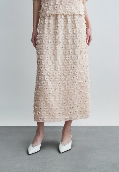 Light pink midi skirt with three-dimensional floral texture, paired with white pointed-toe shoes featuring a lace accent.