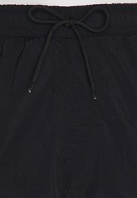 Svart simbyxa i texturerad tyg med elastisk midja och snörning. Har minimal sömnad och en sidficka.
