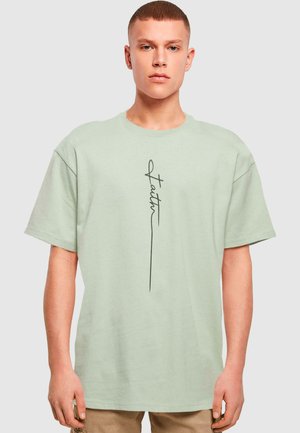 Mintgrøn oversized t-shirt lavet af bomuld, med en sort håndskrevet "Faith" tekstdesign på fronten. Korte ærmer og rund halsudskæring.