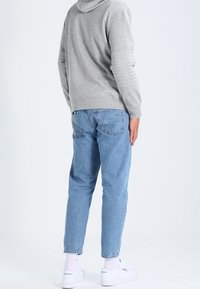 Gray hoodie with a hood, light blue denim jeans, white sneakers, and white socks. The jeans have a relaxed fit and back pockets.