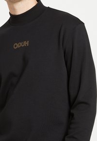 Zwarte lange mouwen coltrui met een slim-fit ontwerp, voorzien van een gouden "HUGO" logo op de borst en een soepele textuur.