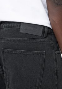 Schwarze Denim-Jeans mit enger Passform, strukturierter Oberfläche, Fünf-Taschen-Design und einem Lederpatch an der Taille mit der Aufschrift "EIGHTYFIVE."