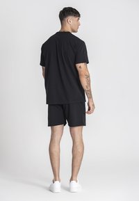 Černá bavlněná souprava trička a šortek s volným střihem. Jednoduchý design s krátkými rukávy, nošeno s bílými teniskami.