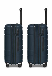 Valigia rigida blu navy con superficie testurizzata, doppia cerniera, dettagli neri, manico retrattile e quattro ruote per la mobilità.