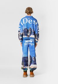 Sudadera azul y pantalones a juego con gráficos de montañas y océano, corte holgado, tejido texturizado y acentos de marca en blanco.
