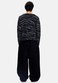 Pull noir et gris duveteux avec un motif à rayures de zèbre, accompagné d'un pantalon noir ample. Vue de dos, détails minimalistes.