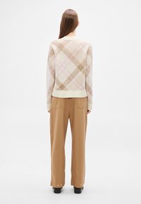 Beežide ja roosade ruutudega kootud kampsun, millel on ümar kaelus, kombineeritud helepruunide laia säärega pükstega ja mustade pahkluu saabastega.