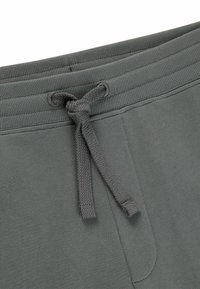 Grijze sweatpants hebben een elastische tailleband met een knoopkoord, een gladde textuur en een eenvoudig ontwerp zonder extra versieringen.