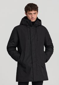 Parka nera imbottita con cappuccio regolabile, chiusura frontale con zip e tasche laterali. Texture liscia e design minimalista.