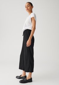 Witte top met korte mouwen, zwarte textuur wijde broek met trekkoord en zwarte loafers. Eenvoudig ontwerp, neutrale kleuren en een relaxte pasvorm.