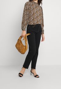 Blusa con stampa floreale e maniche elastiche, jeans skinny neri con orlo sfrangiato, tacchi neri a strappy e borsa a manico nodoso color cammello.