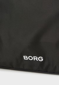Fekete szövet táska, sima textúrával, az elülső részen nagy betűkkel „BORG” felirattal.