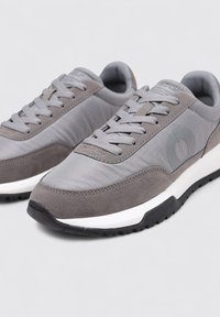 Zapatillas grises con superficies lisas y texturizadas. Presentan un diseño con cordones, un logo sutil en el costado y una entrezona blanca en contraste.