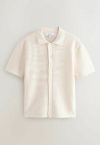 Chemise en maille de couleur crème à manches courtes, avec un col et des boutons sur le devant, présentant un motif perforé horizontal subtil.