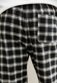 Pantalon de pyjama en tissu à carreaux noir et blanc avec une texture douce, doté d'une taille élastique et d'une poche arrière. Motif à carreaux sur toute la surface.