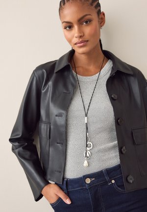 Schwarze Jacke aus Kunstleder mit Kragen, ausgestattet mit Knopfverschluss und einer Brusttasche, kombiniert mit einem grauen, gerippten Pullover und dunklen Jeans.