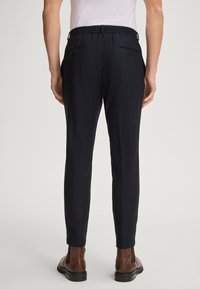 Granatowe, dopasowane spodnie z elastycznym paskiem, dwiema tylnymi kieszeniami i gładką fakturą, zestawione z brązowymi botkami.