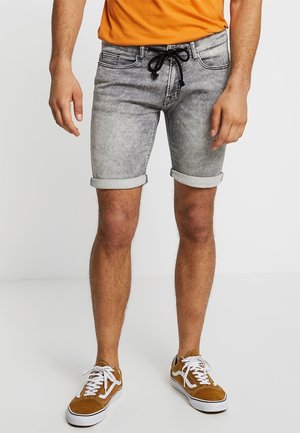 Shorts en denim gris avec des ourlets roulés, dotés d'une taille à cordon. Portés avec des baskets blanches et un t-shirt orange.