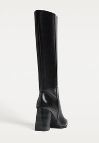 Bottines noires montantes en cuir lisse, dotées d'un talon bloc et d'une silhouette ajustée avec des détails de coutures verticales.