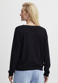 Črn dolg rokav pulover s sproščenim krojem, z širokim izrezom in rebrastimi manšetami, v kombinaciji s svetlož blue džinsami.