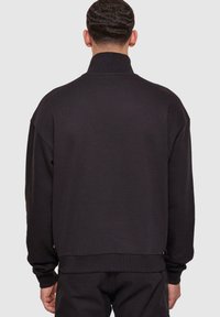 Svart genser med høy krage, løs passform, ribbede mansjetter og nederkant, laget av mykt stoff, med et minimalistisk design.