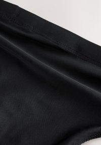 Čierna látka s hladkou textúrou a viditeľným šitím pozdĺž okraja, pravdepodobne časť odevu alebo odevného doplnku.