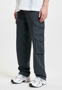 Donkergrijze cargobroek met meerdere klepzakken, recht figuur en een gladde textuur. G gedragen met witte sportschoenen.