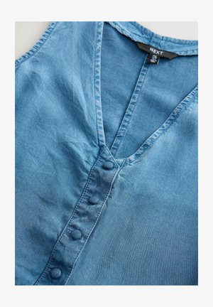 Kergelt sinine teksastopp, millel on V-kaelus, nupuga eesosa ja pehme, tekstuuriga kangas. Lihtne disain ilma mustriteta.