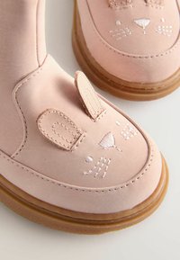 Różowe buty z ekoskóry z wzorem przedstawiającym króliczka, z wyhaftowanymi detalami i teksturowanymi uszami. Gumowa podeszwa o gładkim wykończeniu.