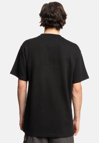 Black short-sleeve t-shirt made from textured fabric, featuring a straight cut and back seam detail. No visible logos or embellishments.