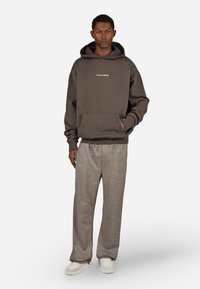 Tmavo sivá mikina s klokaním vreckom a predným logom, v kombinácii s svetlohnedými širokými nohavicami s textúrou a bielymi teniskami.