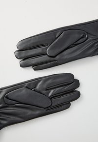 Een paar zwarte leren handschoenen plat gelegd met de duimen die overlappen op een witte achtergrond.