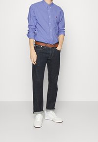 Niebieska koszula w kratę z guzikami, ciemne dżinsy, brązowy sk órzany pasek i białe sneakersy. Casualowy styl z podwiniętymi rękawami i mankietami.