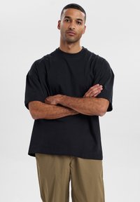 Sort bomulds t-shirt med afslappet pasform, korte ærmer og rund halsudskæring, parret med khaki bukser. Glat tekstur, ensfarvet, uden mønstre.