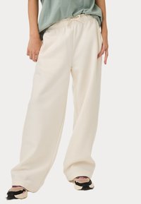Losse crème kleurige sweatpants met een elastische tailleband en zijzakken. Draagbaar met zwarte en roze sneakers. Zachte textuur.
