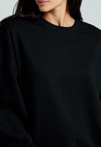 Fekete kapucnis pulóver bordázott kerek nyakkal és ejtett vállú kialakítással. Az anyag lágy és texturált. Nincsenek látható minták vagy díszítések.