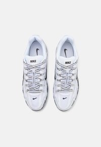 Sneakers albe Nike din materiale din plasă și sintetic, cu un sistem de amortizare la talpă, accente negre și șireturi etichetate pentru un fit sigur.