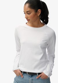 Witte langslavige T-shirt van zachte katoen, met een ronde hals en ribgebreide manchetten. Een klein logo is weergegeven op de linkerborst.