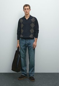 Tmavý svetr s argyle vzorem, modré džíny, hnědé semišové boty a tmavá taška. Hladká textura, uvolněný střih a ležérní styl.