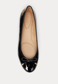 Μαύρη παρτινέ μπαλέτα με στρογγυλή μύτη, μικρή λεπτομέρεια με φιόγκο και χρυσή διακοσμητική λεπτομέρεια στο πλάι. Η εσωτερική επένδυση είναι μπεζ.