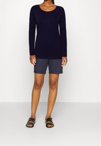 Långärmad marinblå tröja, grå shorts med veckad fåll och svarta sandaler. Slät textur, avslappnad passform och enkel design.