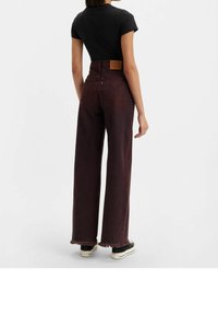 Jeans burdeos de cintura alta con corte recto, dobladillo deshilachado y un parche de cuero marrón en la parte trasera de la cintura. Combinados con una camiseta negra.