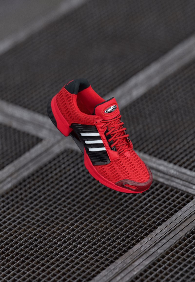 Red athletic shoe with mesh upper, black accents, textured design, and black sole, featuring white stripes and a branded tongue.