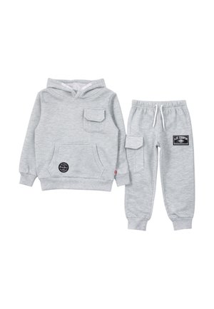 Sweat à capuche gris clair avec poches avant et poitrine, assorti à un pantalon de jogging avec poche latérale et logos de la marque.