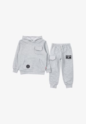 Sweat à capuche gris clair avec poches avant et poitrine, assorti à un pantalon de jogging avec poche latérale et logos de la marque.